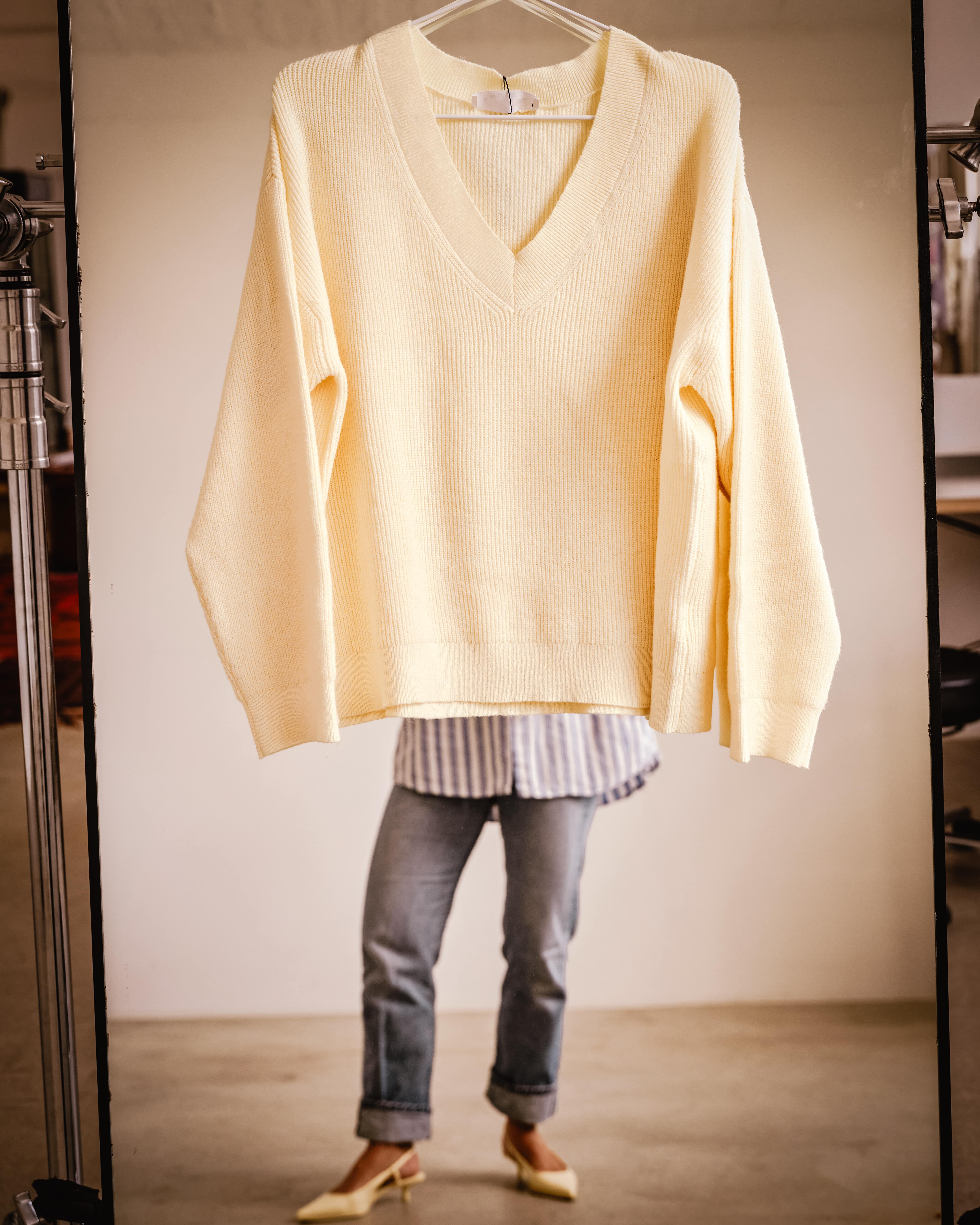 Woman looking in mirror with sweater on hanger in front of her
